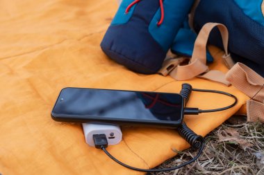 Akıllı telefon taşınabilir şarj cihazıyla şarj ediliyor. Sırt çantalı bir uyku tulumunda cep telefonu olan bir elektrik bankası.