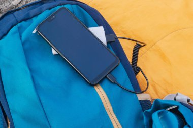 Akıllı telefon taşınabilir şarj cihazıyla şarj ediliyor. Sırt çantalı bir uyku tulumunda cep telefonu olan bir elektrik bankası.
