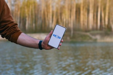 Adam elinde elinde bedava kablosuz ağ ikonu olan bir akıllı telefon tutuyor. Telefon ormanın ve gölün arka planında. Doğada ücretsiz internet erişimi