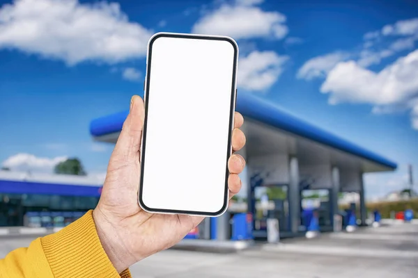 Ein Mann Hält Vor Dem Hintergrund Einer Tankstelle Ein Smartphone — Stockfoto