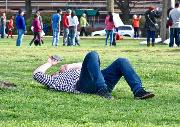 Мужчина лежит в парке и смотрит на телефон. — стоковое фото