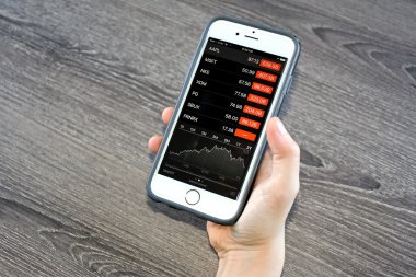 Hisse senedi fiyatları gözden geçirirken bir iphone tutan kişi