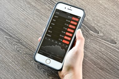 Hisse senedi fiyatları görüntülerken bir iphone tutan