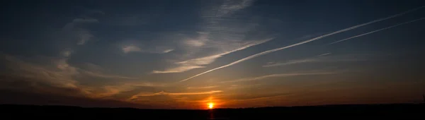 Panorama of the setting spring sun over a field at dusk Stock Photo