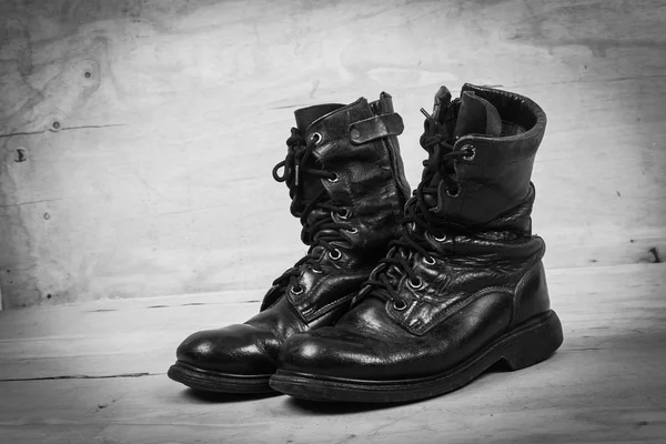 Botas de combate preto velho em fundo de madeira, tom preto e branco — Fotografia de Stock