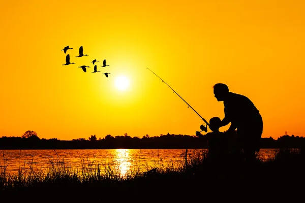 Отец и сын рыбачат на фоне заката реки — стоковое фото