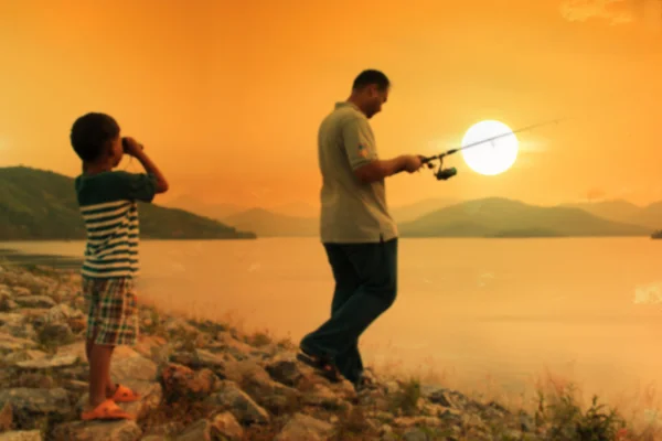 Borrão de menino olhando pai pesca pôr do sol fundo — Fotografia de Stock