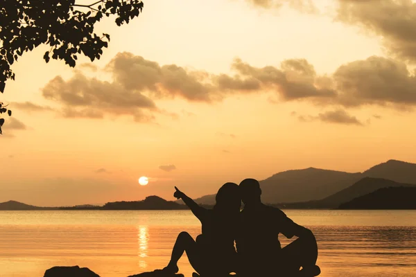 Silhueta de casal de romance sentado em uma rocha ao pôr do sol — Fotografia de Stock