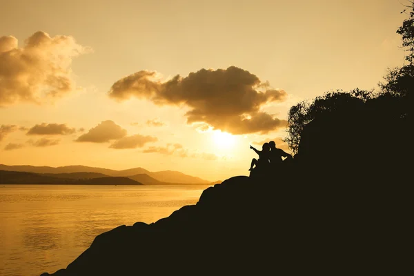 Silhueta de casal de romance sentado em uma rocha ao pôr do sol — Fotografia de Stock