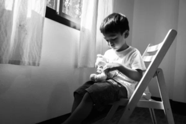 Borroso de niño sentado solo en la silla en la ventana de la habitación, b —  Fotos de Stock