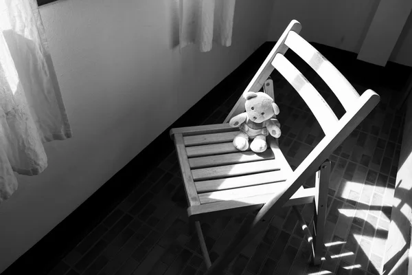 Søt teddybjørn som sitter alene på en stol nær vinduet, svart og hvisk – stockfoto