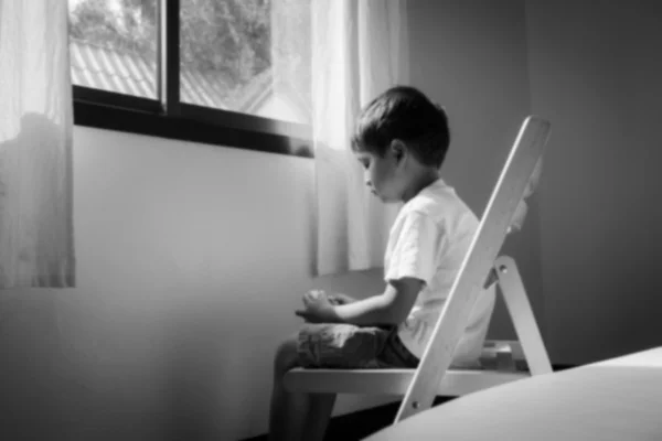 Suddiga lille pojken sitter ensam på stol vid fönstret i rummet, b — Stockfoto