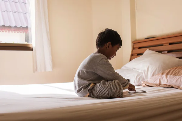 Маленький мальчик сидит на кровати играть смартфон в спальне — стоковое фото