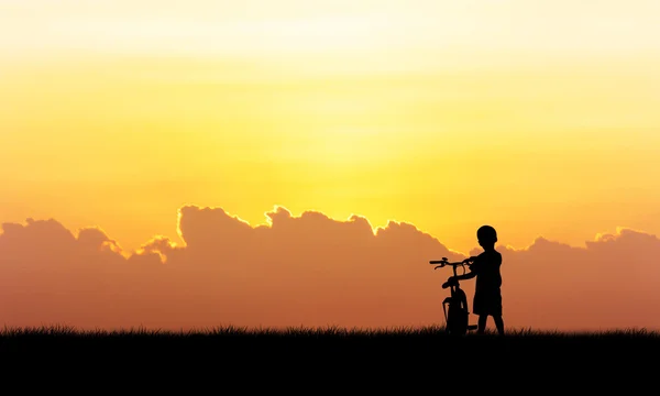 Sylwetka mały chłopiec stojący trzymać rower tło zachód słońca — Zdjęcie stockowe