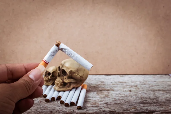 Mano che tiene sigaretta rotta sul cranio Tabacco sigarette su woo — Foto Stock