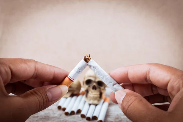 Mano che tiene sigaretta rotta sul cranio Tabacco sigarette su woo — Foto Stock