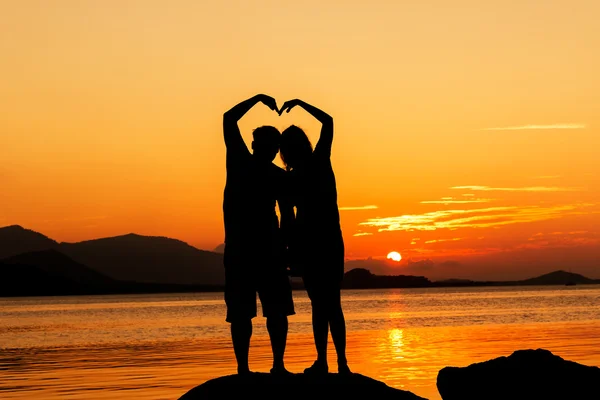 Coppia romantica che fa forma di cuore con le braccia sfondo tramonto — Foto Stock
