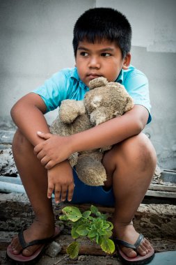 Boy poor with old teddy bear sitting on old wood pile clipart