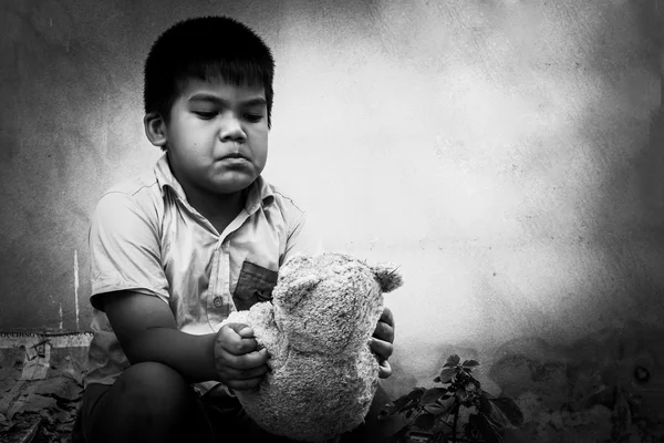 Bambino povero con vecchio orsacchiotto seduto vicino al muro di cemento — Foto Stock