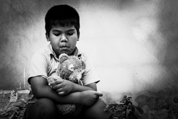 Niño mendigo con viejo osito de peluche sentado cerca de la pared de hormigón —  Fotos de Stock