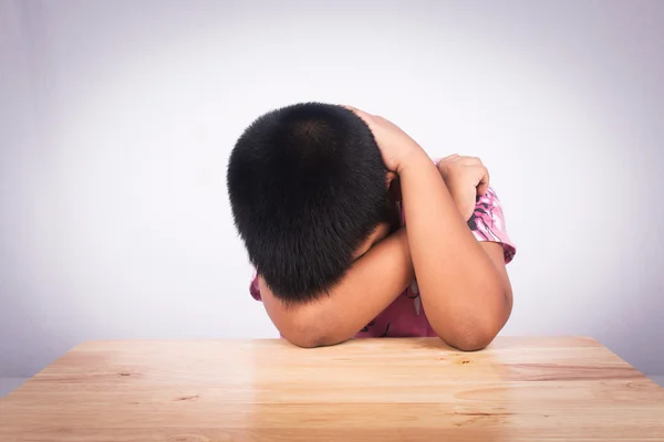 Menino triste situando sozinho na mesa de madeira — Fotografia de Stock