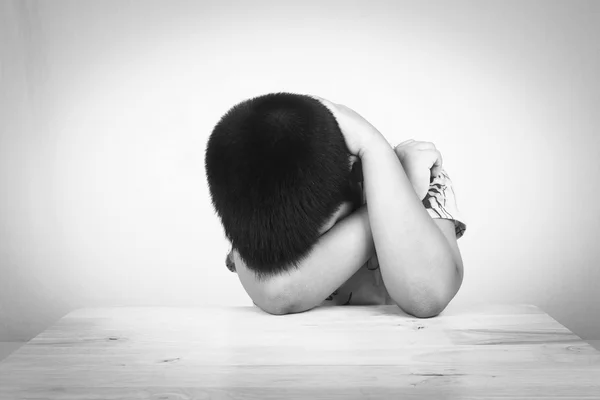 Menino triste situando sozinho na mesa de madeira, preto e branco — Fotografia de Stock