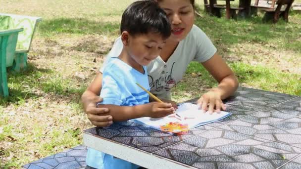 Madre ayudar a su hijo haciendo la tarea en el parque — Vídeos de Stock