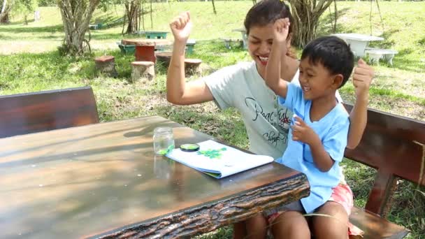 Madre ayudar a su hijo haciendo la tarea en el parque — Vídeos de Stock