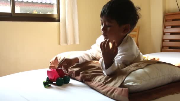 Cute little boy playing toy car on the bed in room — Stock Video