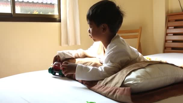 Cute little boy playing toy car on the bed in room — Stock Video