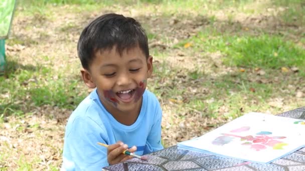 Schattige kleine jongen spelen verf op gezicht in het groene park — Stockvideo