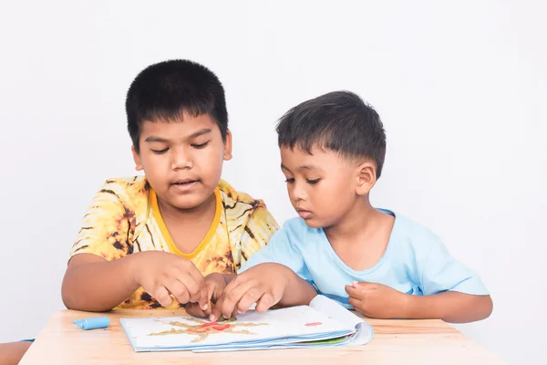 Два маленьких хлопчика грають глину на книзі на білому тлі — стокове фото