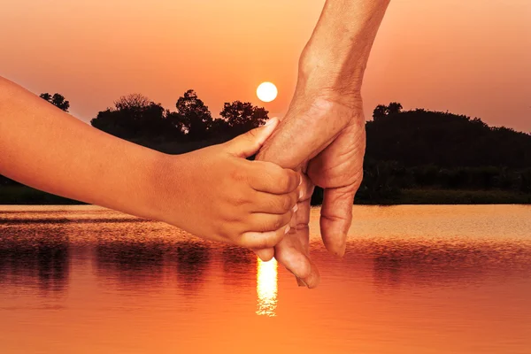 Mano pequeño niño agarre mano viejo hombre al atardecer río fondo — Foto de Stock