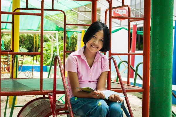 Aranyos ázsiai lány olvasni a könyvet, a játszótér — Stock Fotó