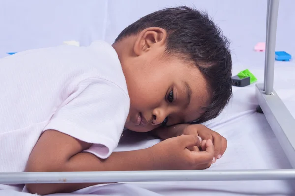 Un petit garçon asiatique couché sous la table sur fond blanc — Photo