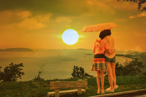 Mãe e filha de pé alcançar um guarda-chuva pôr do sol fundo — Fotografia de Stock