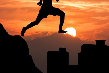 silhouette of young man jumping from the mountain to the buildin clipart
