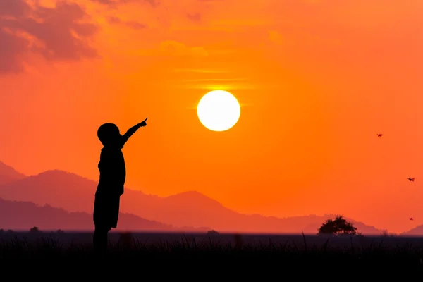 Siluett av asiatiska pojke pekar till solen vid solnedgången bakgrunds — Stockfoto