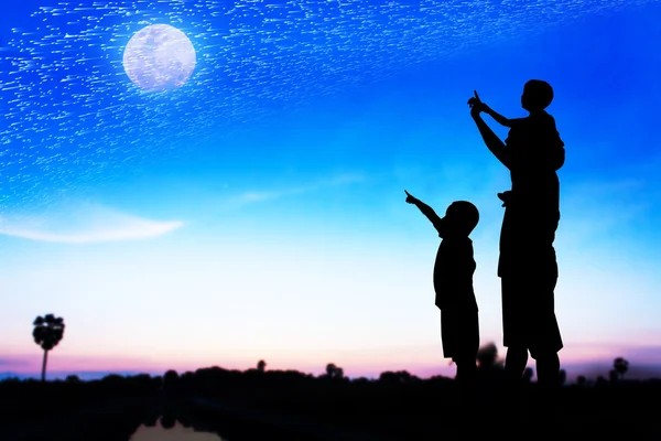 Silueta de padre uso mano punto su hijo mirar a la luna llena en — Foto de Stock