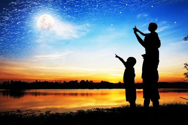 Silueta de padre uso mano punto su hijo mirar a la luna llena en — Foto de Stock