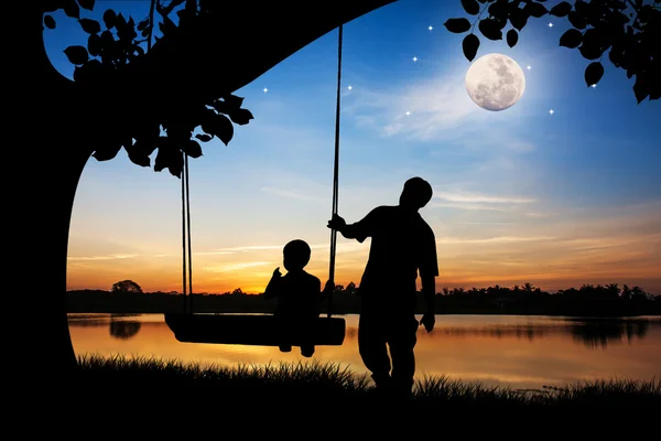 Силует батька і сина грають гойдалки під великим деревом повний — стокове фото