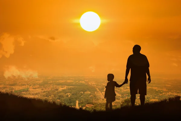 Baba ve oğul kasaba günbatımı backgro üzerinde duran silüeti — Stok fotoğraf