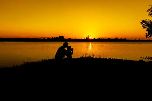 Madre giocare suo figlio a fiume tramonto sfondo — Foto Stock