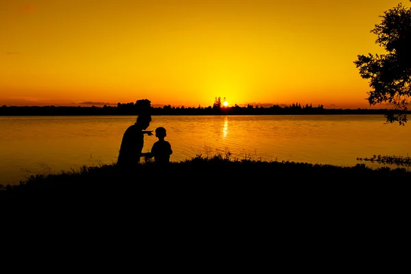 Mãe jogar seu filho no rio pôr do sol fundo — Fotografia de Stock