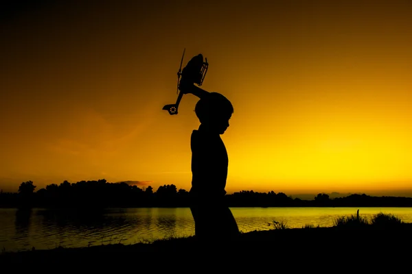 Menino jogar helicóptero brinquedo no rio pôr do sol fundo — Fotografia de Stock