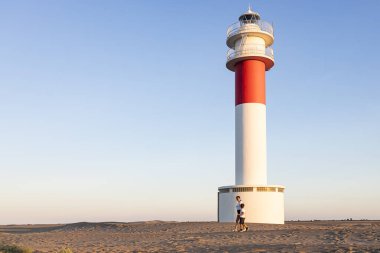 Anne ve oğul güzel bir deniz fenerinin yanında yürüyorlar.