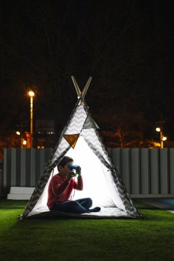 Geceleri Kızılderili çadırında dürbün kullanan küçük bir çocuk.