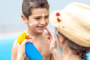 Anne bir yaz gününde oğluna güneş kremi sürüyor.