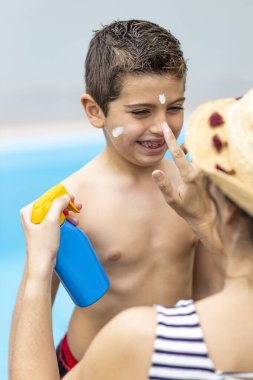 Anne bir yaz gününde oğluna güneş kremi sürüyor.