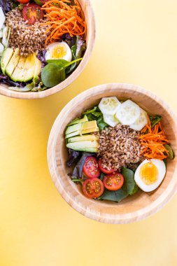 Havuç, yumurta, salatalık, avokado, domates ve kuzu marullu esmer pirinç salatası. Üst Manzara. Sarı arkaplan.